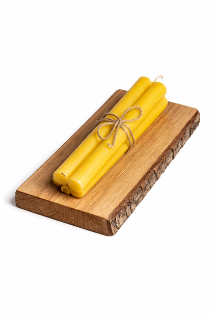 Two tall handmade beeswax yellow candles tied with twine on a wooden board against a white background