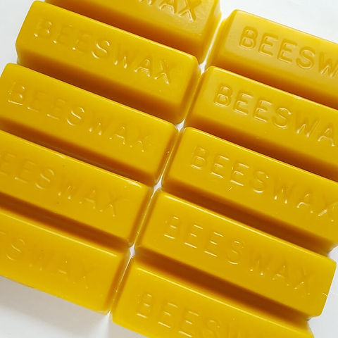 Yellow beeswax bars with 'BEESWAX' embossed on them, arranged on a white background.